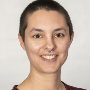 Emily Progin has close cropped dark hair, dark eyes, and a silver nosering.