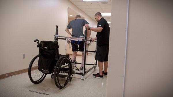 an individual walking in a frame with their wheelchair behind them