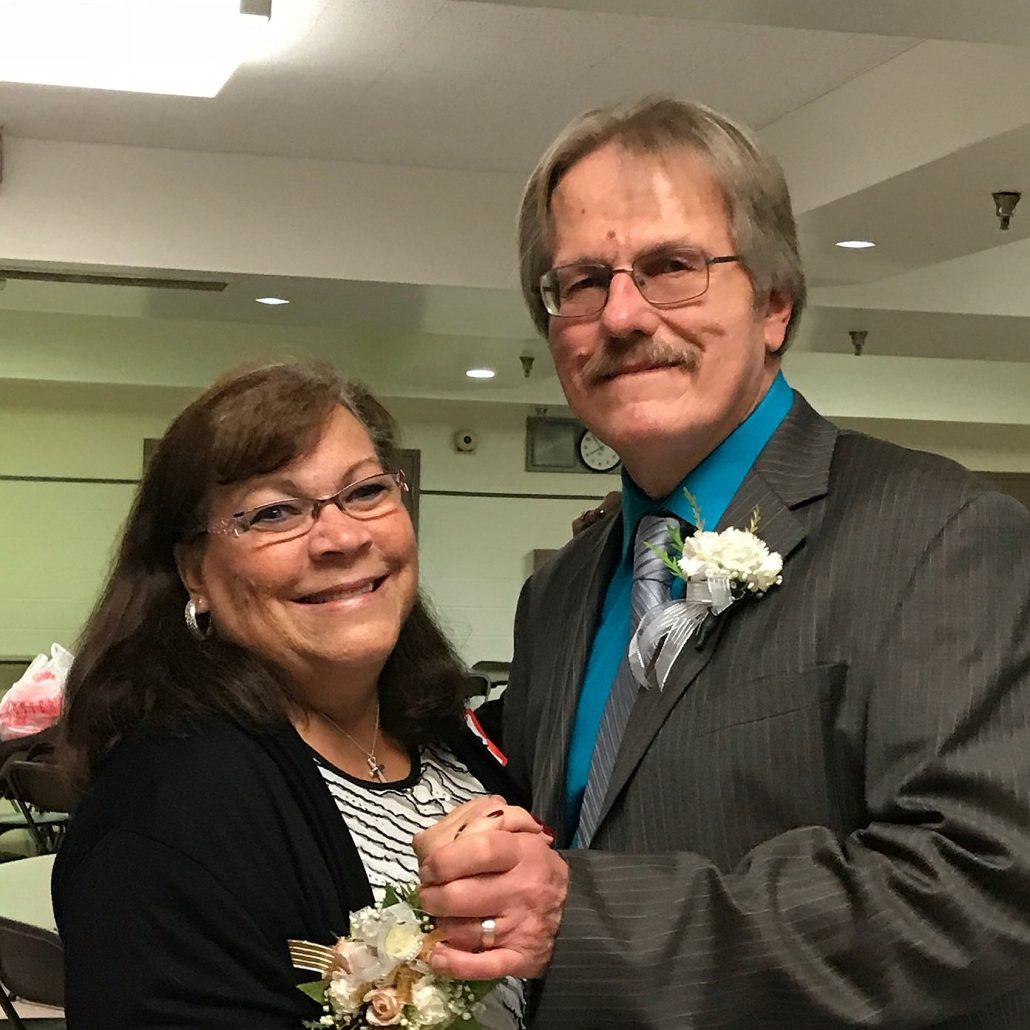 A husband and wife hold hands and smile.