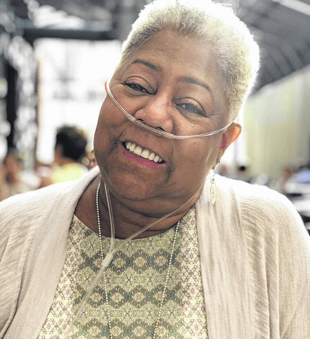 Double lung transplant recipient Julie Posey is pictured pre-transplant with an oxygen tube. She has brown skin, short curly gray hair, and a big smile.