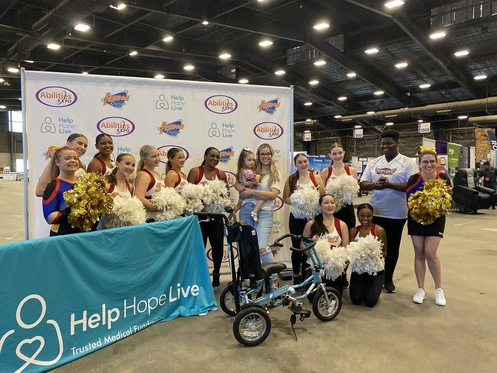 Emberly Lindsey receives a Freedom Concept adaptive bike from Help Hope Live at Abilities Expo with cheerleaders.