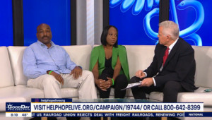 Brianna and her father Brian sit on a white couch as they are interviewed by a FOX29 reporter. Dad Brian has brown skin, a light blue button-up shirt, and khaki pants with a dark mustache and a bald head. 33-year-old Brianna wears a green cutaway jacket over black pants and has brown skin and shoulder-length straight black hair. A ticker at the bottom from FOX 29 shares Brianna's Help Hope Live Campaign Page URL and Help Hope Live's phone number.