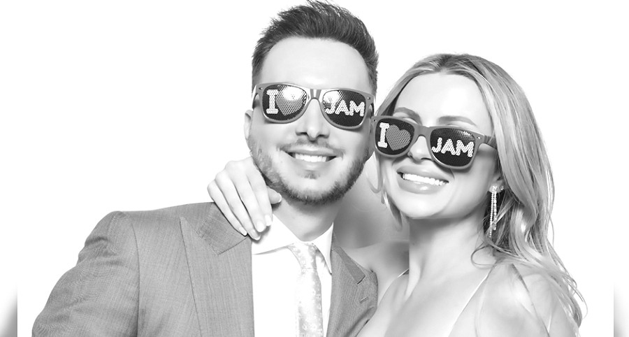 In a grayscale photo at aspireLIFE's annual JAM fundraiser, George and his female guest wear I Heart Jam sunglasses and formal attire with big smiles.