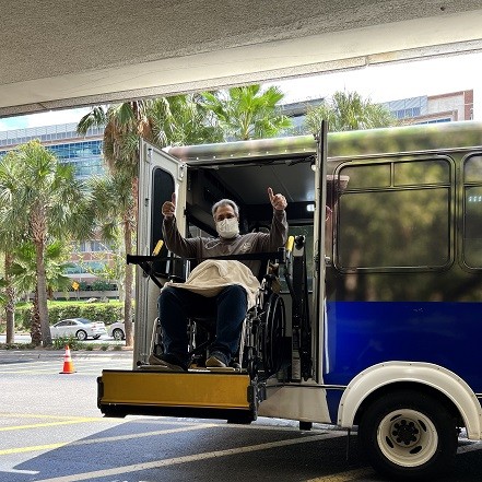 Liver transplant recipient Alfonso Larocca gives the thumbs up wearing a mask as his whelchair is lowered down from a bus.