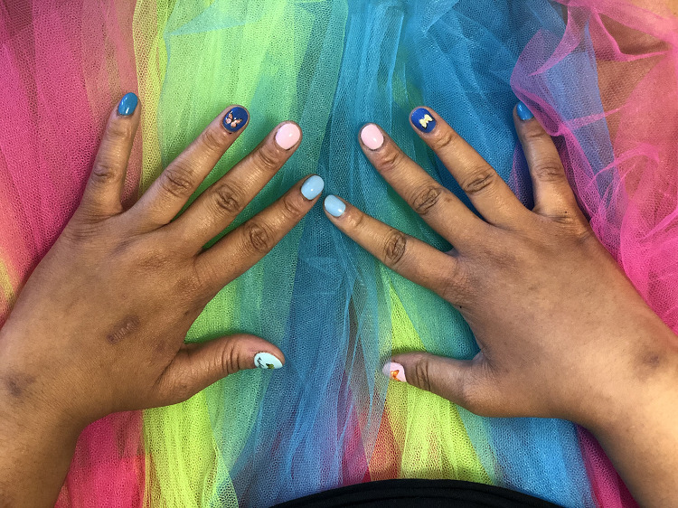 Keisha's hands are light brown with elaborately painted nail as they rest on a rainbow tulle skirt.