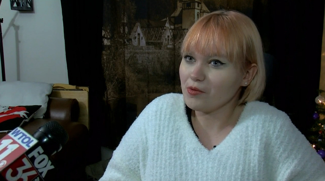 Alivianna Gallup is being interviewed in this screenshot. The 17-year-old has light skin, light blue eyes, and winged eyliner with a shoulder-length dyed bob and a white sweater.