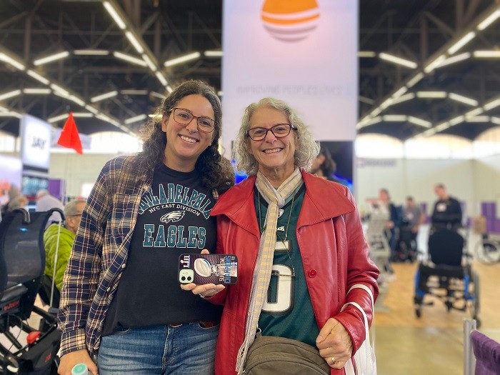 Two smiling female presenting Abilities Expo Dallas attendees both have curly hair and tortoiseshell glasses and Eagles gear in dark green and white.