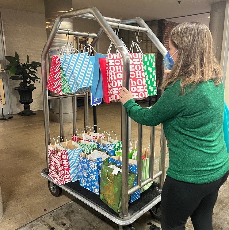 Help Hope Live's Sonny Mullen wears a green sweater and a mask as she rolls a bellhop cart full of colorful Bags of Hope, ready for delivery.