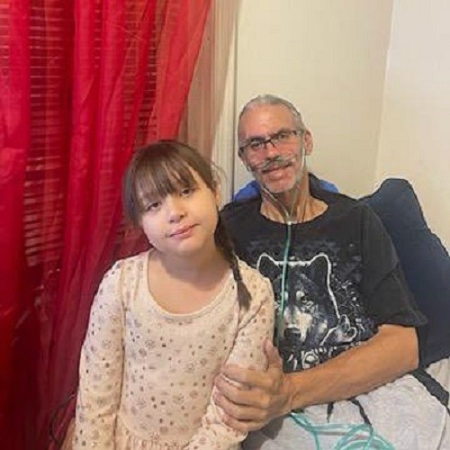 Luis Torres Gonzalez is pictured pre-double lung transplant with an oxygen tube attached to his nose. He has light brown skin and long gray hair in a ponytail with glasses. He is pictured with a smiling child with brown hair in a braid.