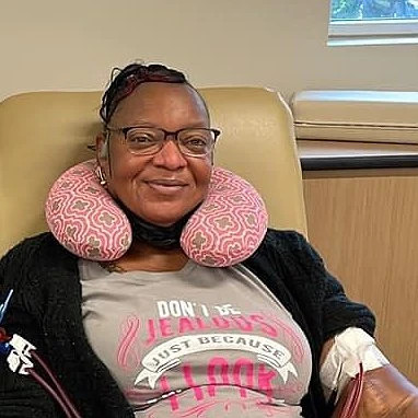 Kidney transplant recipient Patrina Devane is pictured pre-transplant hooked up to a dialysis machine with a neck millow. She has brown skin, black hair, and glasses.