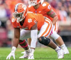 Clemson's KJ Henry wears his bright orange football uniform. He has brown skin.