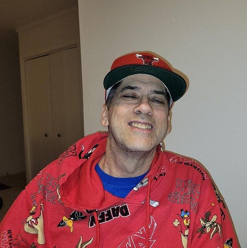 Kidney transplant recipient Mark has light skin, a big smile, black eyebrows, a red Chicago Bulls ball cap, and a red cartoon-print hoodie.