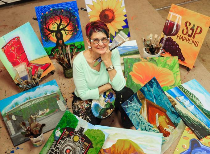 Before her paralyzing surgery, artist Judy Grossman is pictured on the floor surrounded by her colorful paintings. She has light skin, short red-black hair, and glasses. Her art is in turn whimsical, bold, colorful, and mystical.