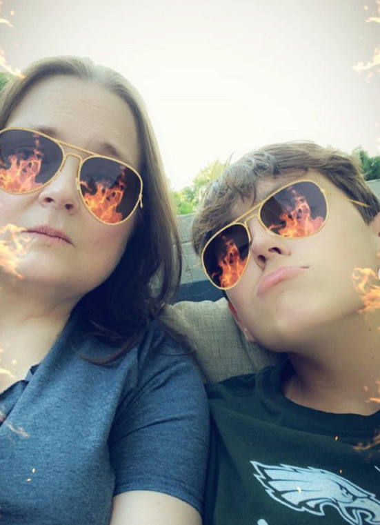 In a funny social media selfie, Linda Jara and a young family member use a filter that gives them both aviator sunglasses with animated flames. Linda has light skin and brown hair. Her young family member has light skin and short brown hair and a Philadelphia Eagles t-shirt.