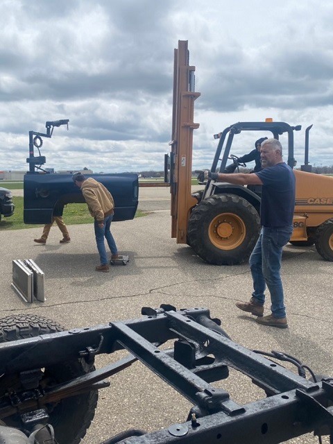 Construction in progress on Frank's adaptive vehicle. An outdoor photo of heavy metal framework, a small forklift, and several men at work.