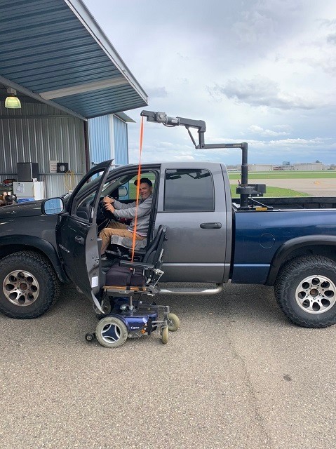 Frank is seated in his modified adaptive truck outside with his mobility device next to him, ready for a transfer.