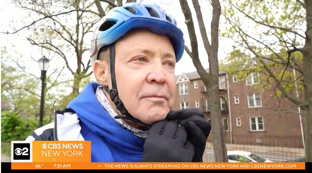 Jerry Cahill adjusts his blue bike helmet outdoors with black-gloved hands. He has light skin, gray hair, and light eyes.