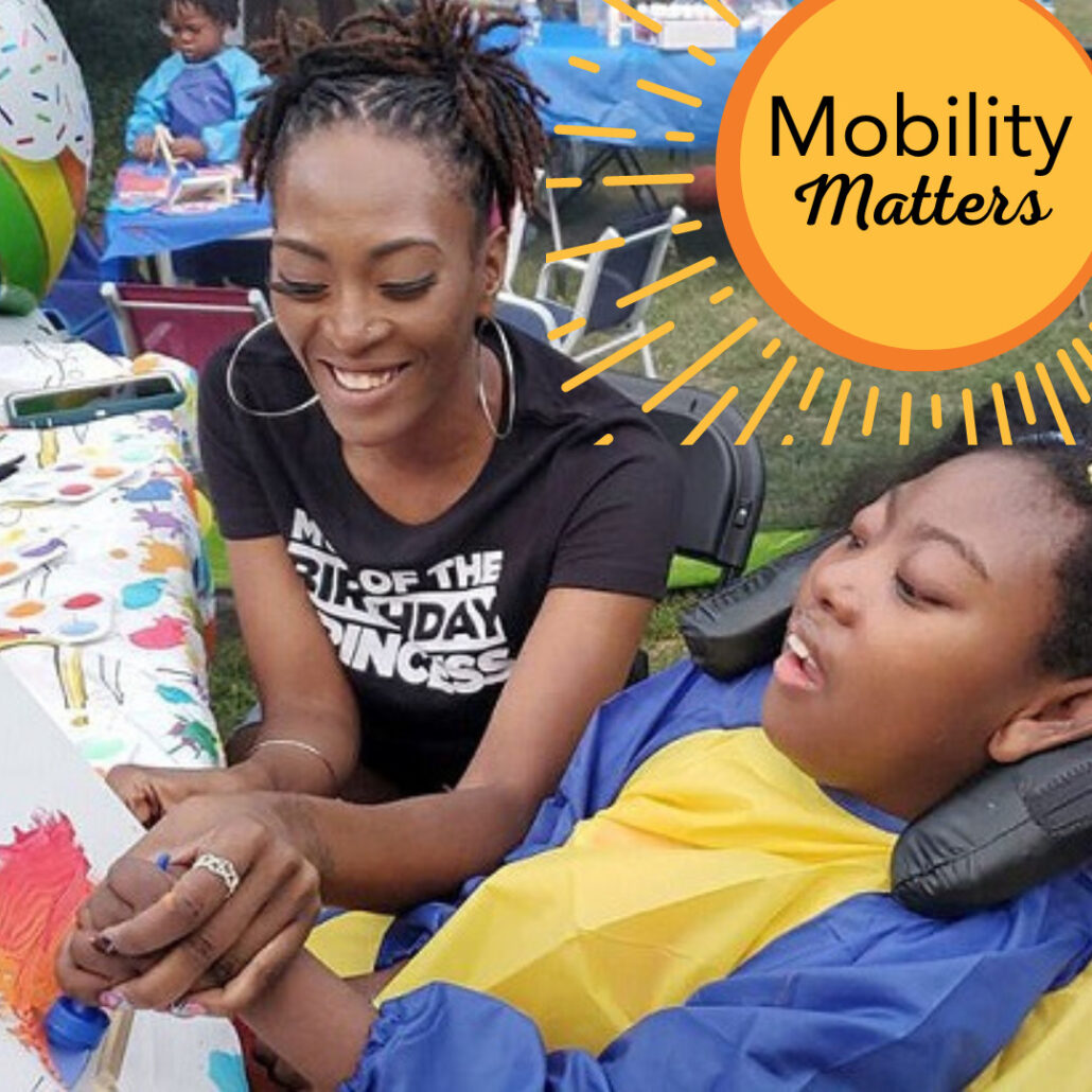 Mom Sierra Dillard holds her daughter Zoë's hand to help her paint at a birthday party activity. Sierra has brown skin, a black t-shirt, braided hair, and hook earrings. Zoë has brown skin and curly black hair. She sits in a supportive mobility device. A graphic button reads Mobility Matters with a sunburst graphic.