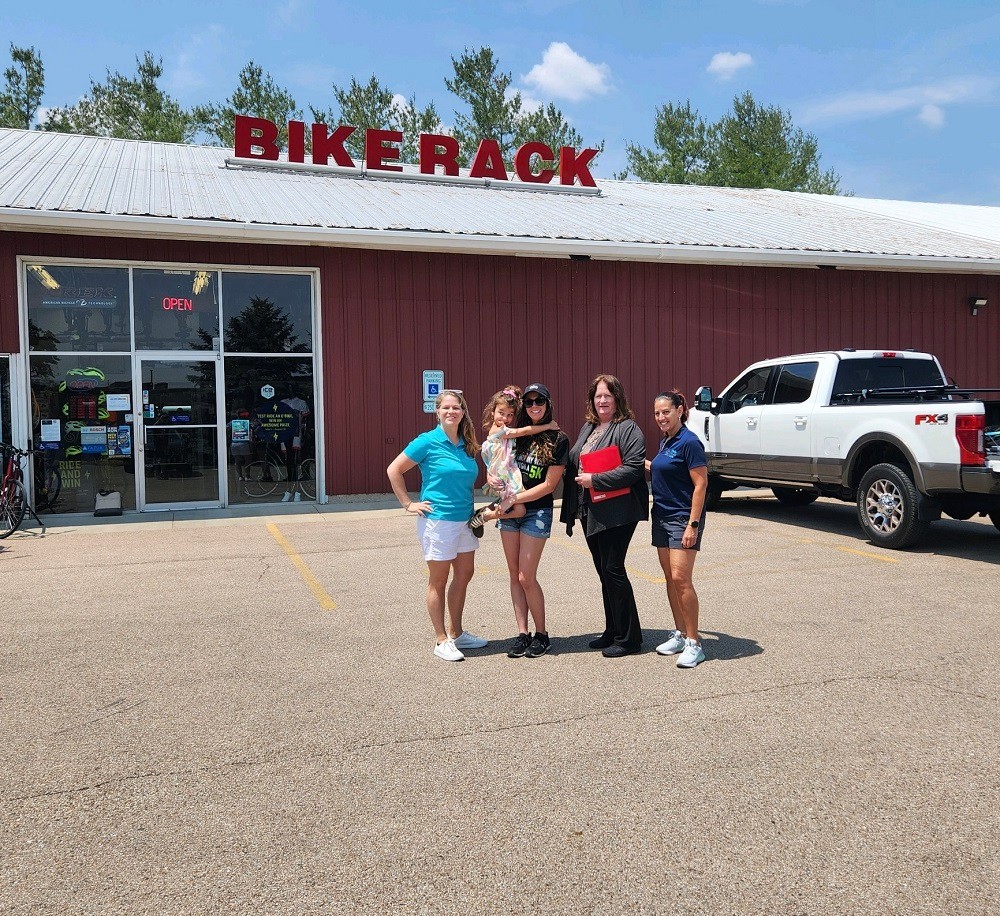 Outside of The Bike Rack in Chicago, Sonny Mullen and Kelly Green from Help Hope Live stand with Tammy Simmons and her daughter Katherine, co-founders. Katherine holds a young girl in her arms.