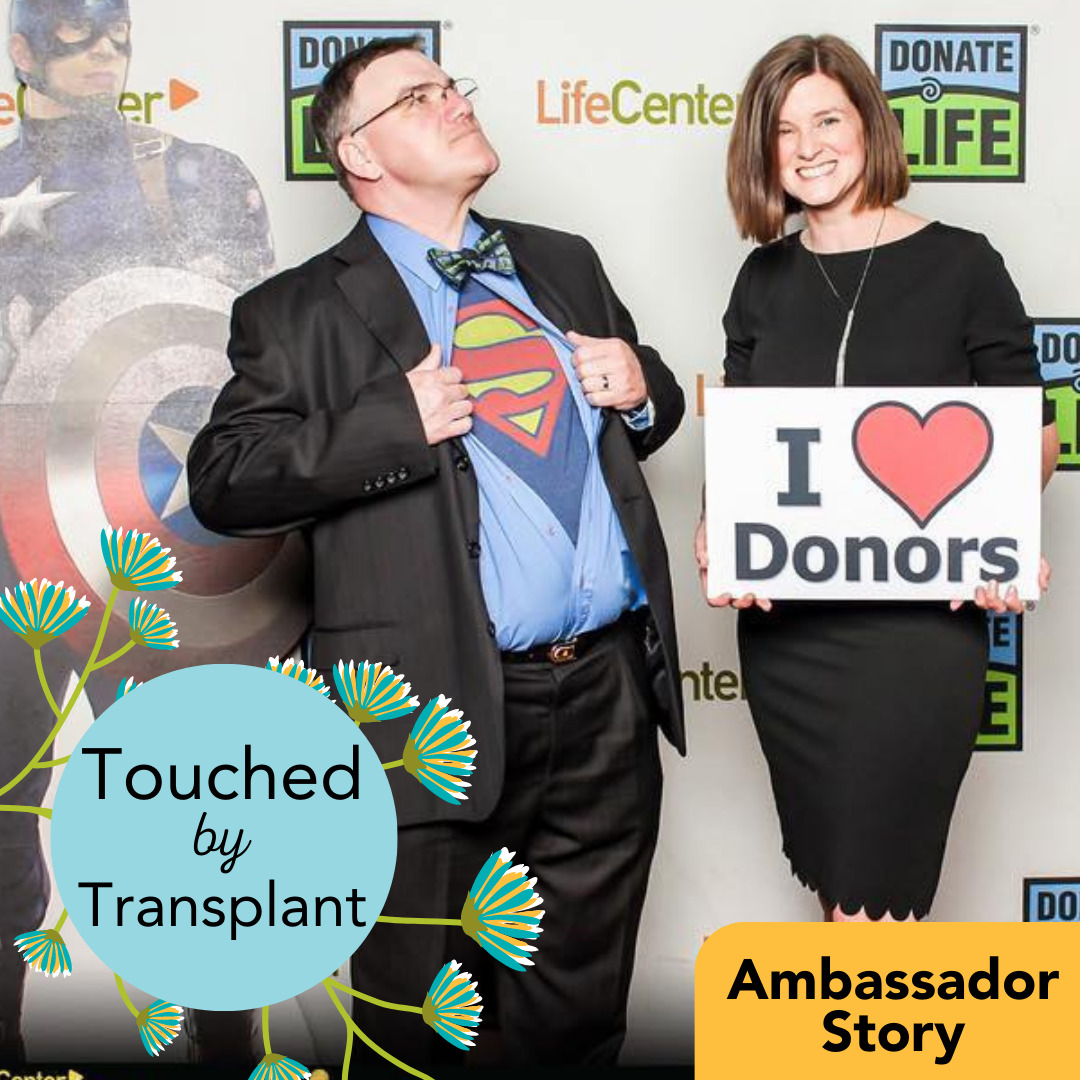 A graphic reads Touched by Transplant Ambassador Story. Heart transplant recipient Pat McEntee and his wife Amy are standing in front of a Donate Life step-and-repeat banner with a life-size cardboard cutout of Captain America. Pat opens his button-up shirt to reveal a Superman logo t-shirt. He has light skin, short dark hair, and glasses. Amy holds a sign that says I Heart Donors and wears a black professional dress. She has light skin and shoulder-length straight brown hair.