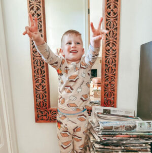 Three-year-old Zeke Clark is pictured pre-amputation giving peace signs at home. He has light skin, short brown hair, and a smores themed pajama set.