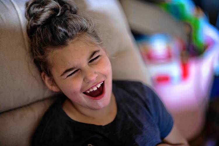 In a photo provided by the Concord Monitor, 8-year-old Lila Coe is smiling with an open mouth. She as light skin, dark hair pulled up into a bun, and a navy t-shirt.