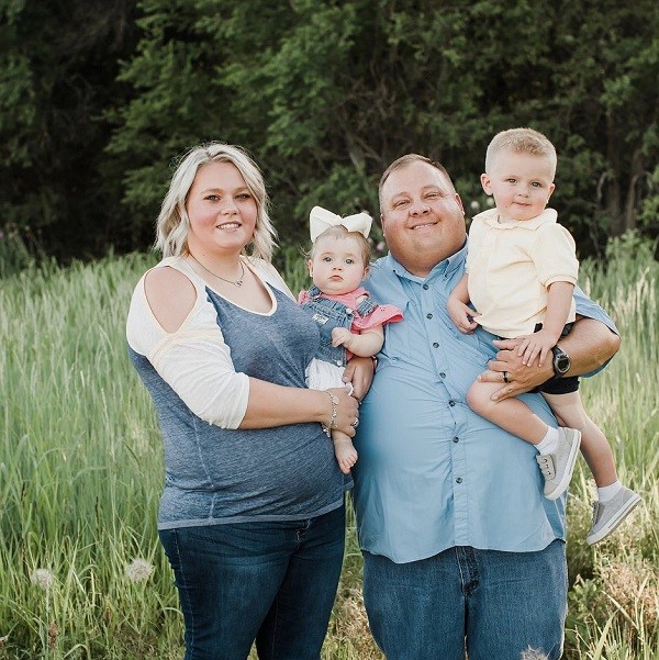 Matt Nix with his wife and two young children, one toddler girl and one young boy, in an outdoor family portrait. Matt has light skin and short hair, and his wife has light skin and blonde hair to her shoulders.