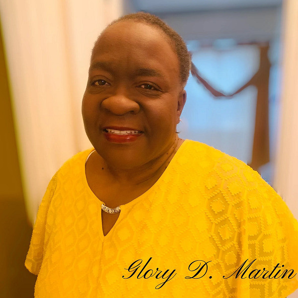 Glory's photo is labeled with text Glory D. Martin in cursive. Glory has brown skin, brown eyes, red lipstick and short-cropped gray-brown hair. She wears a bright yellow blouse.