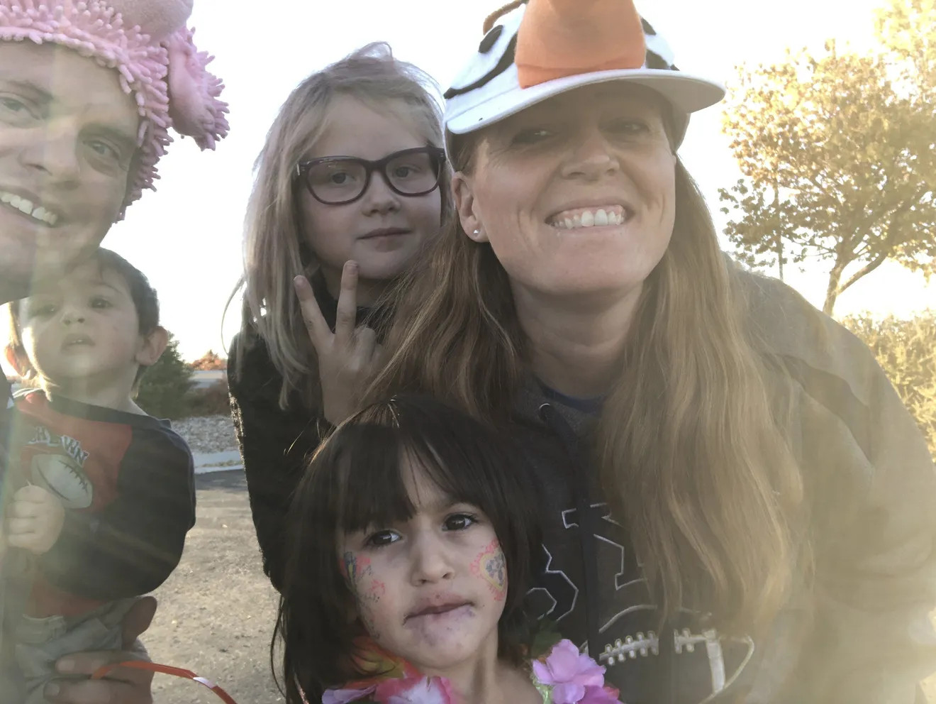 Erin Merkley with her husband Michael and three children, ranging in age from 1 to 9 years old. Erin has light skin, sandy brown hair past her shoulders, and a homemade snowman face ball cap hat. Her husband has light skin and blue eyes and wears a textured pink floppy hat. He holds their youngest son who has light skin and short brown hair. One daughter is with Rrin with dark near-black straight hair and bangs. Behind her, eldest daughter has light skin, blonde hair past her shoulders, and black rimmed glasses.