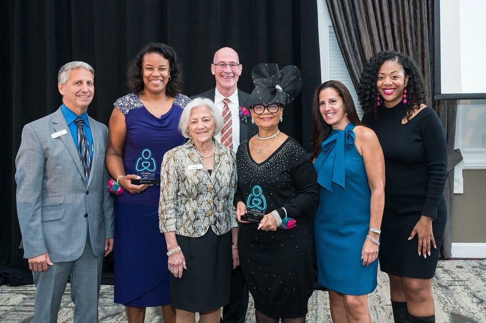 The 2023 Live It Up! award recipients Nicole Henry, Brad Marsh, and Rev. Dr. Lorina Marshall-Blake with co-founder Patricia Kolff, Executive Director Kelly L Green, emcee Cherri Gregg, and board member Ron Siggs. All are in formal attire in a carpeted ballroom setting.