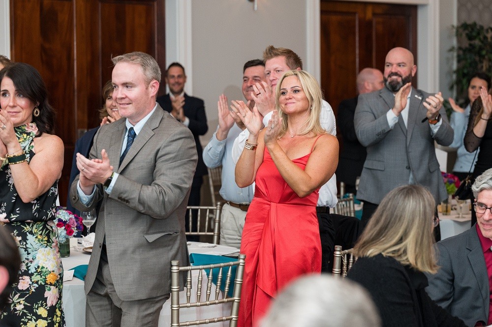 The guests at the 2023 Live It Up! gala give a standing ovation next to their tables. They are dressed in suits or cocktail dresses.