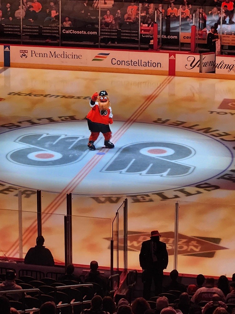 Philadelphia Flyers mascot Gritty skating in the middle of the ice during a Flyers game. He is a big orange monster.