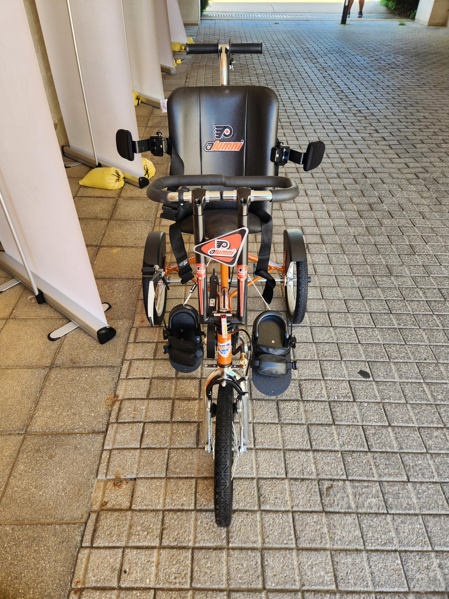 A three-wheel adaptive bike from Freedom Concepts in Flyers-themed orange and black colors.