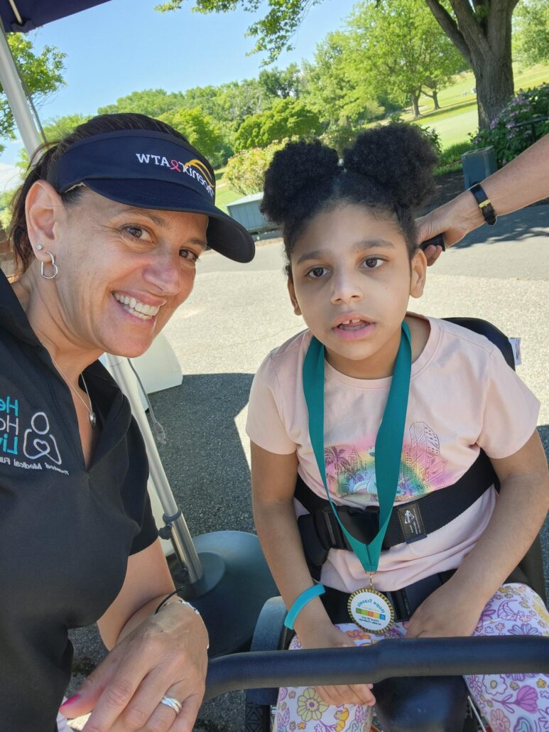 Help Hope Live Executive Director Kelly L Green with adaptive bike recipient Josie Johnson. Josie is 8 years old and has light brown skin and curly dark hair in afro puffs. Kelly has light skin and hazel eyes.