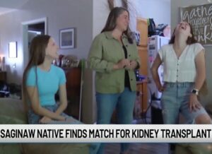 23-year-old Rylee Wobio is pictured with her future kidney donor Hannah Nicklyn and her mother in their home in a screenshot from a TV interview. The ticker reads Saginaw Native Finds Match for Kidney Transplant.