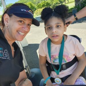 Help Hope Live Executive Director Kelly L Green with adaptive bike recipient Josie Johnson. Josie is 8 years old and has light brown skin and curly dark hair in afro puffs. Kelly has light skin and hazel eyes.