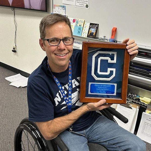 Philip Brady seated in his wheelchair holding an educator award.