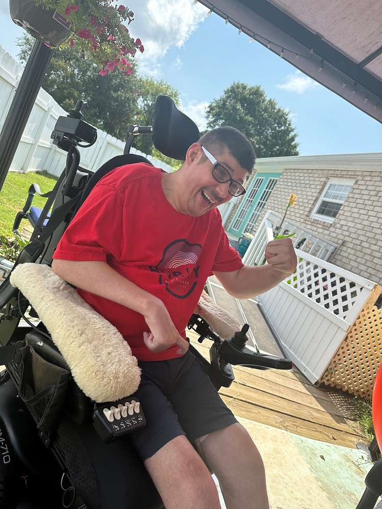 41-year-old Gerald Avant seated in his black power chair smiling outside of a home with a ramp.