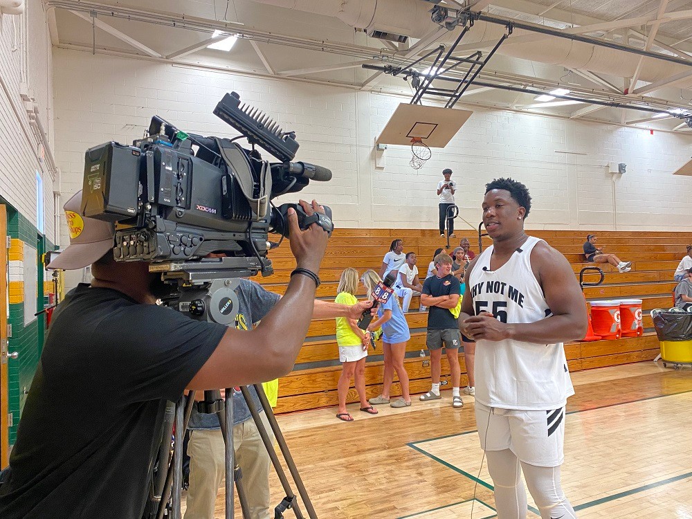 Washington Commanders player KJ Henry interviewed by a TV crew on a basketball court.