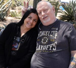 Larynx transplant recipient Marty Kedian gives his wife Gina bunny ears as they both sit on a park bench in a desert environment.