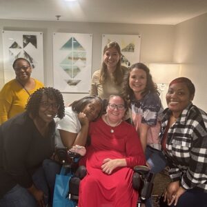 Jennifer Jenkins seated in her power chair surrounded by seven friends.