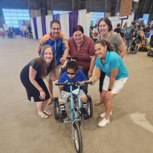 Freedom Concepts and Help Hope Live staff surround 12-year-old Favio on his new adaptive bike at Abilities Expo Phoenix in 2024.