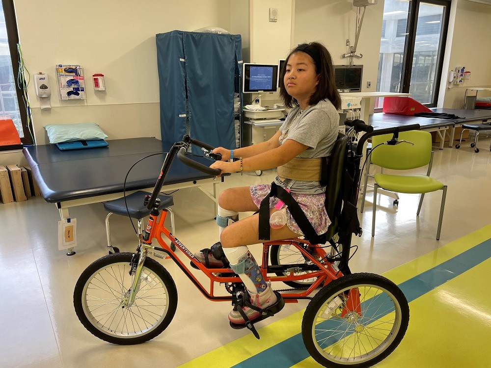 16-year-old Jinju rides a three-wheel adaptive bike in therapy.