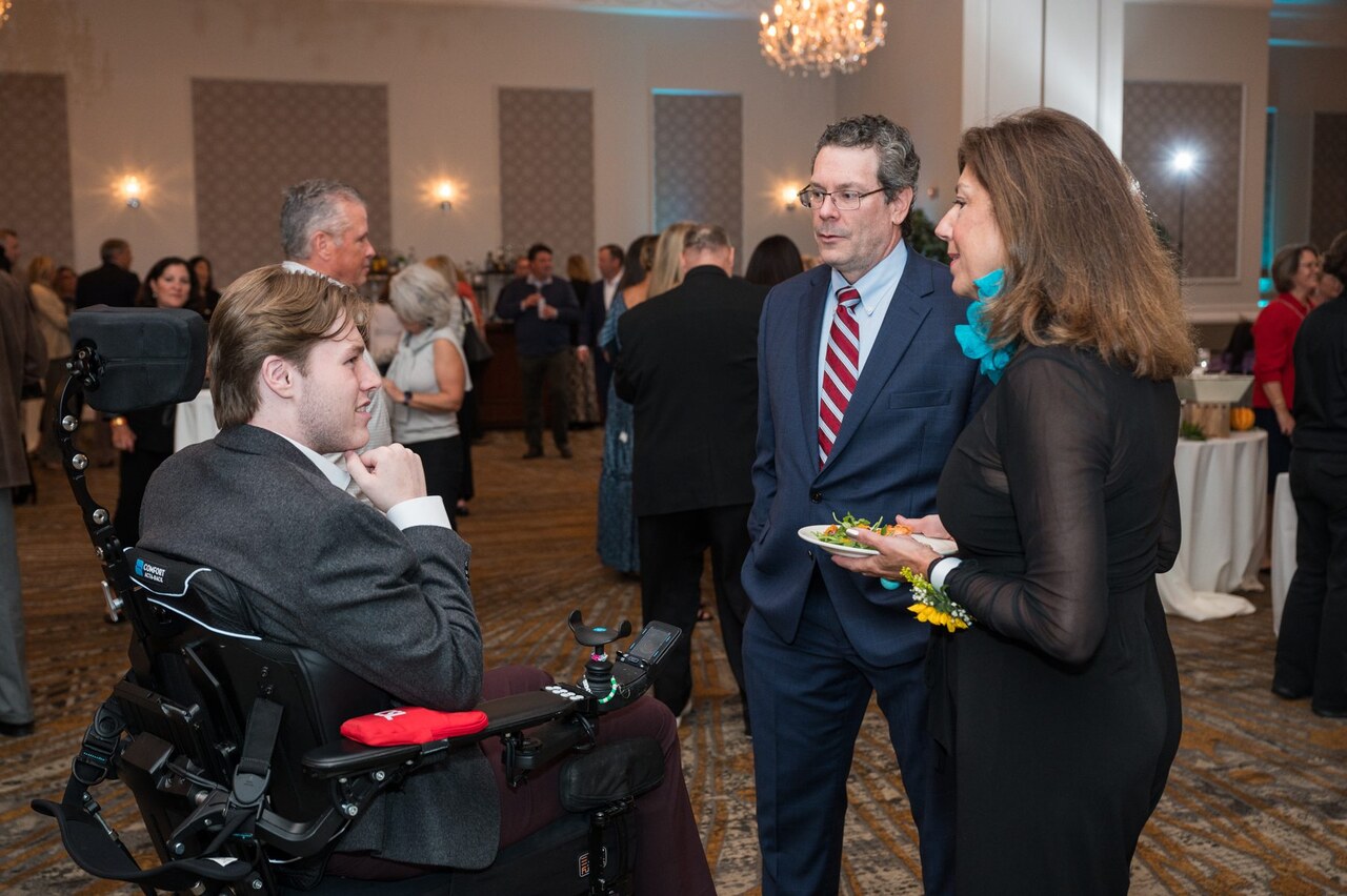 Pat Hoey in his power chair and father Ed Hoey speaking to Stephanie McAlaine at the 2024 Live It Up! gala supporting Help Hope Live.