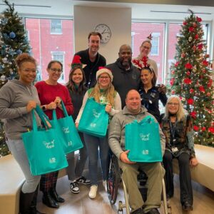 Help Hope Live staff and Magee Rehab staff hold Bags of Hope in a holiday photo for 2024.