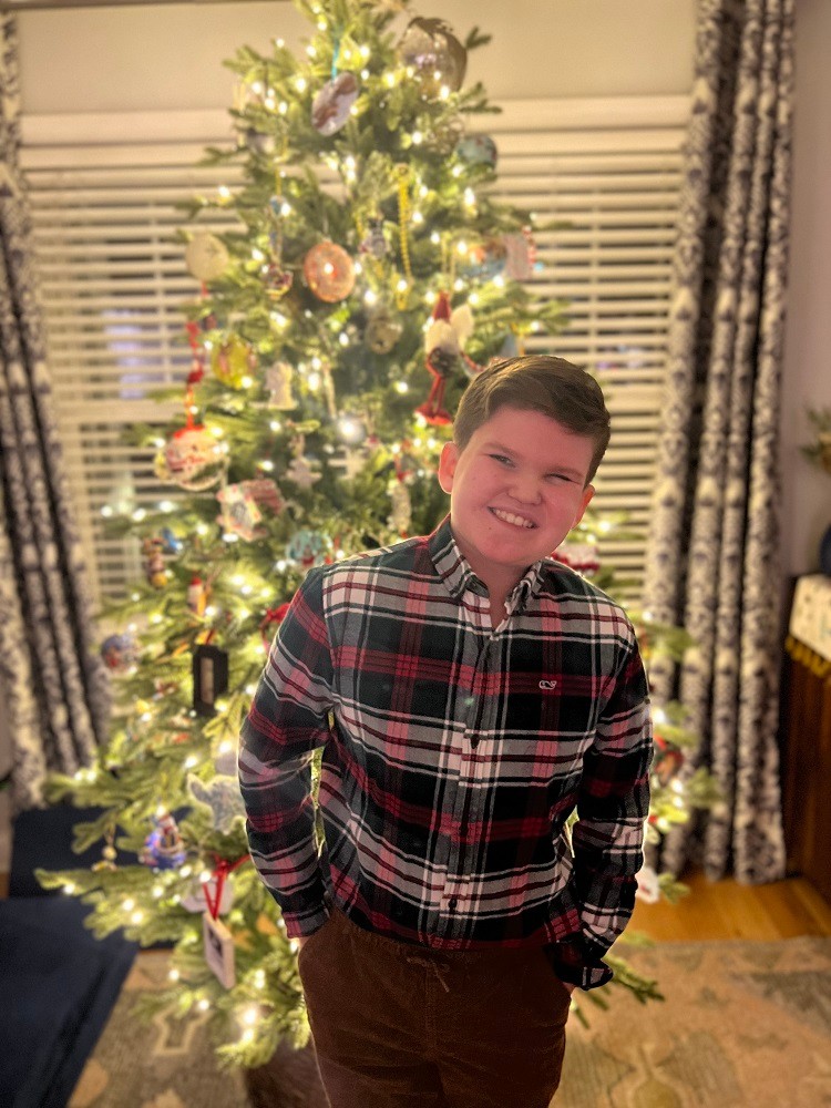 12-year-old Tommy Schrank stands in front of a Christmas tree.