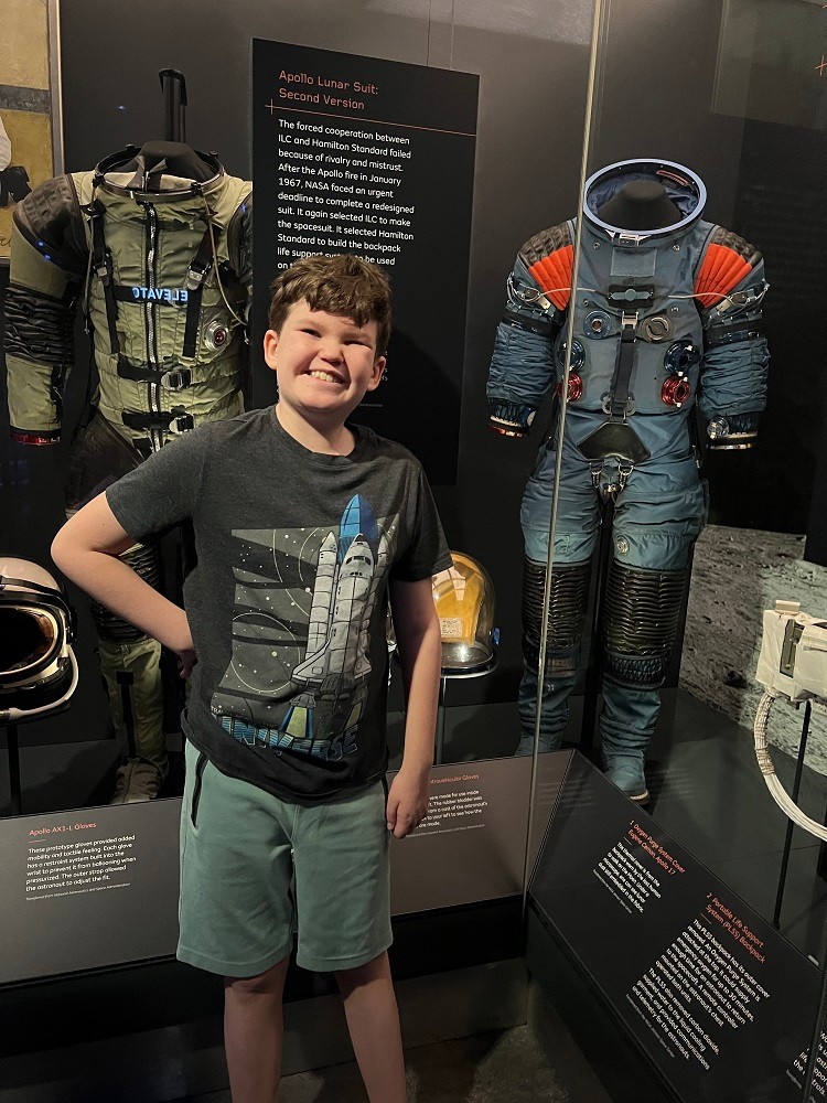 12-year-old Tommy Schrank poses in front of a NASA space suit exhibit.
