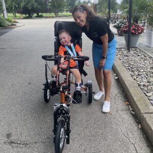 Kelly L Green with a grinning 3-year-old Sidney Schmid as he rides his new Flyers themed custom bike. July 2025.