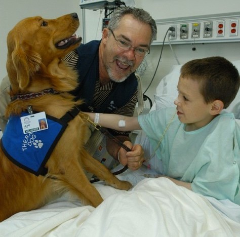 Photo of William Scott Baggett visiting a child in the hospital with his therapy dog Lavie.