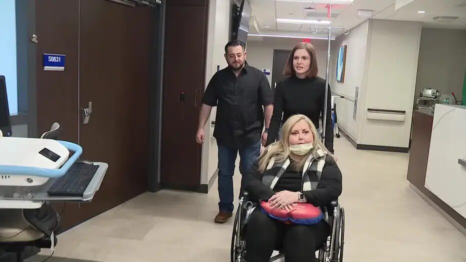Angela Maples is seated in a wheelchair in the hospital being pushed by kidney donor Amanda McCowen and Angela's husband Joshua,